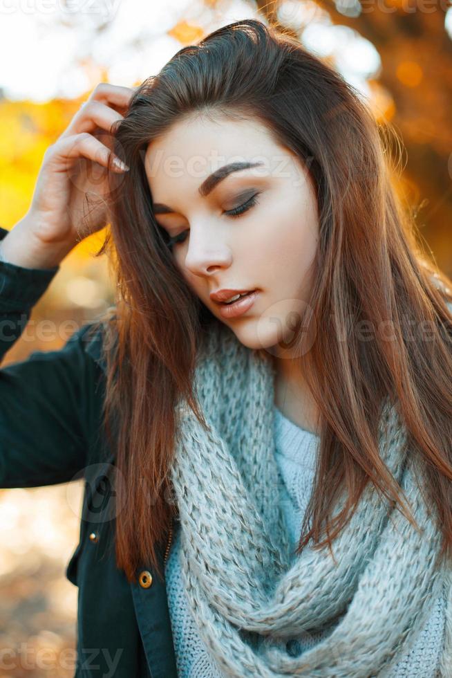 Close-up portrait of a young beautiful girl in knitted sweater, scarf and a black jacket in the autumn park photo