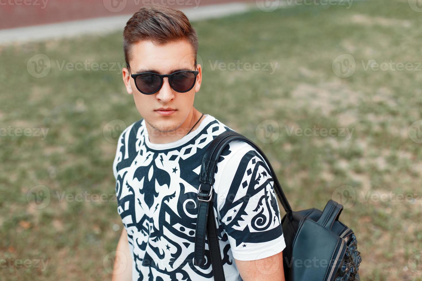 joven apuesto con gafas de sol caminando con una bolsa foto