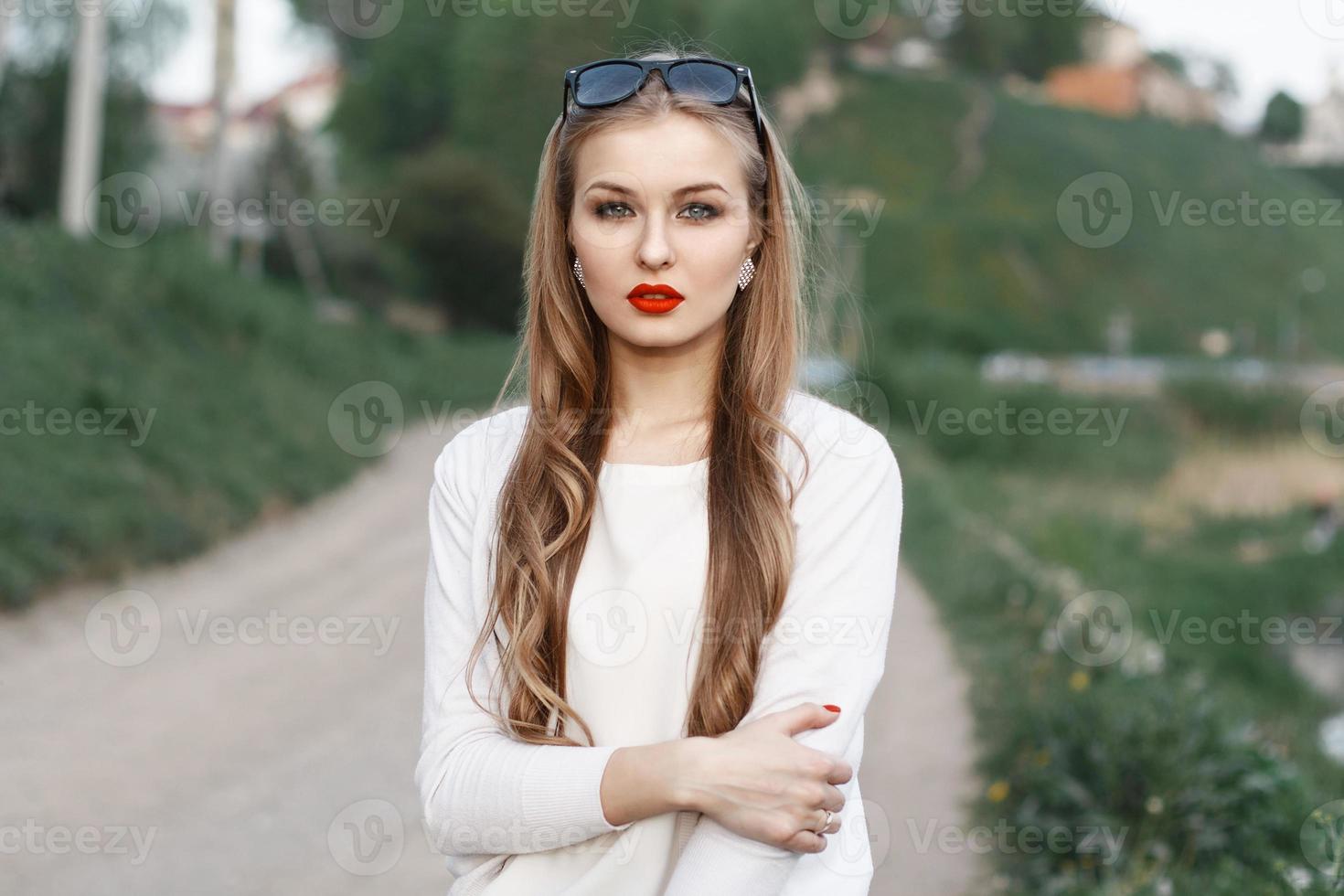 hermoso retrato de una mujer joven con labios rojos y gafas de sol. en el fondo de la carretera y los campos verdes. tiempo de primavera foto