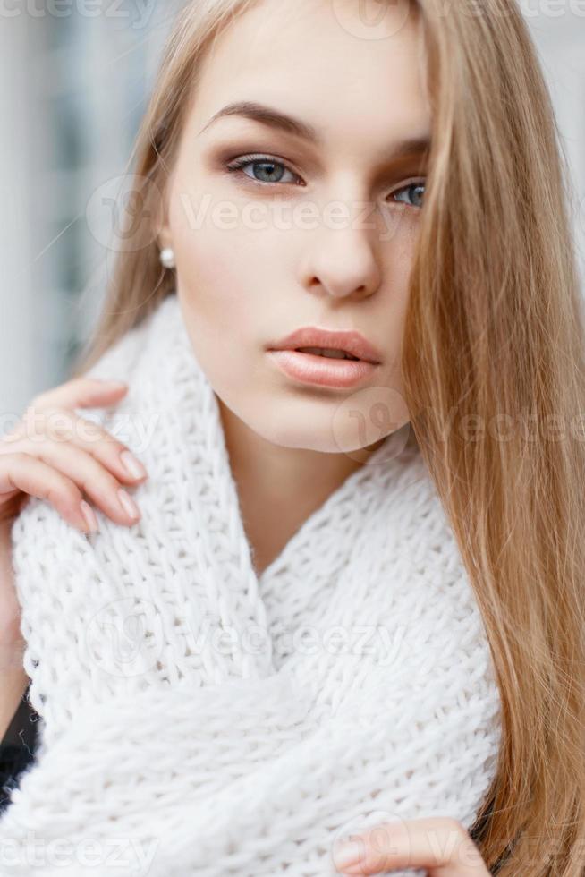 Close-up portrait of a beautiful woman with a white knitted scarf on a background of an autumn day photo