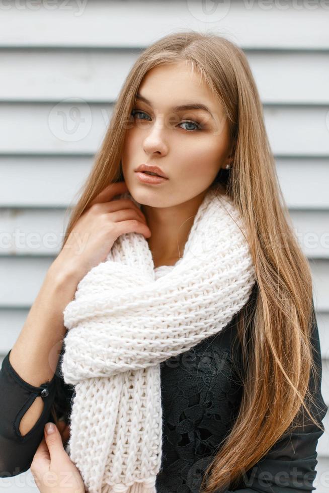 Young beautiful girl in a white knit scarf and a black dress on a background of a wooden wall photo