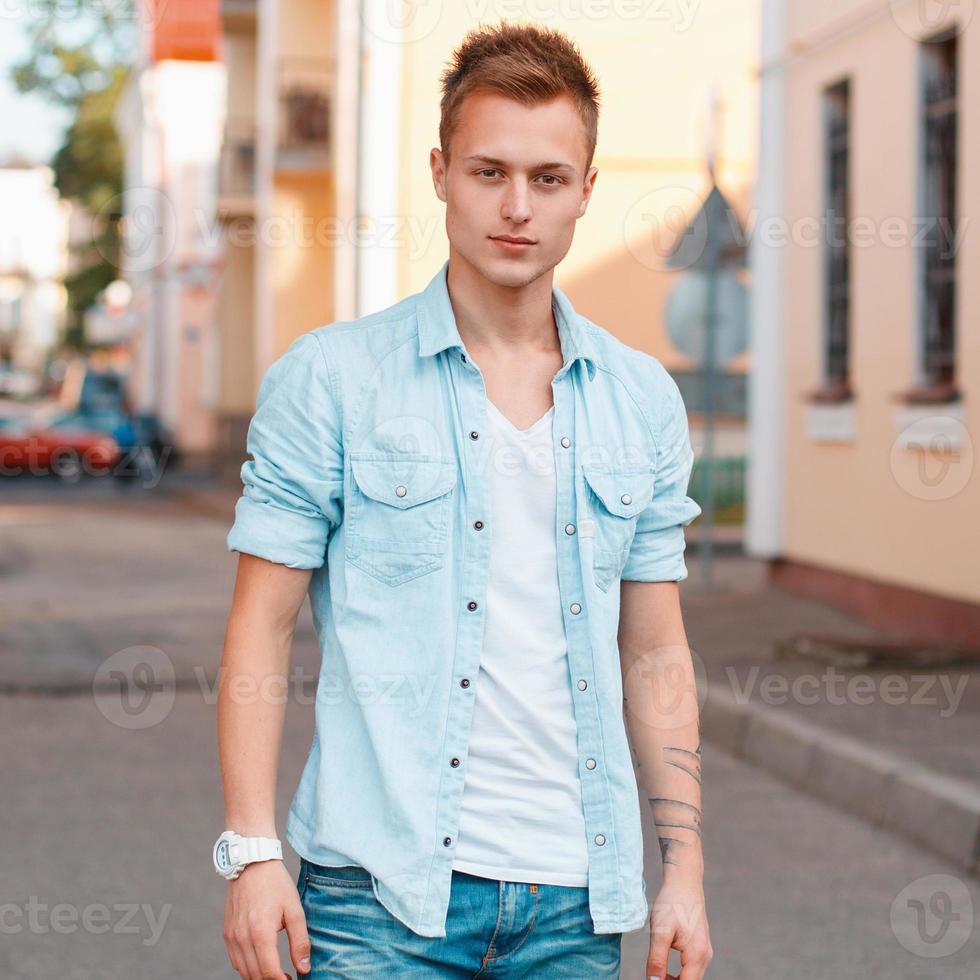 joven apuesto en una camisa de mezclilla y jeans en el fondo de la ciudad. foto