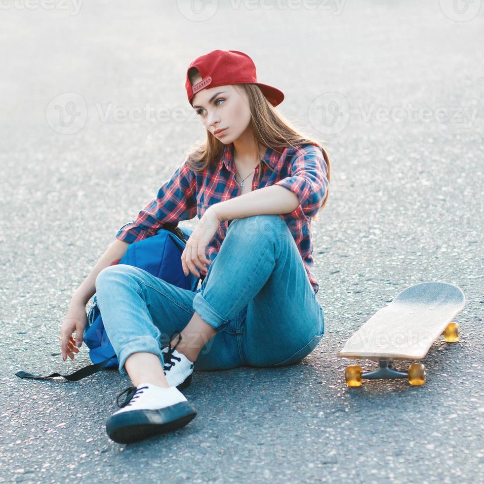 Portrait of a beautiful woman in a shirt and a baseball cap with a skateboard in the park. photo