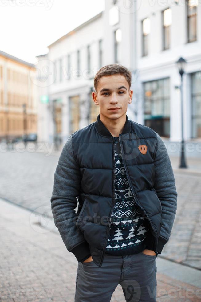 Young handsome man in winter clothes standing near the building, holding hands in pockets photo