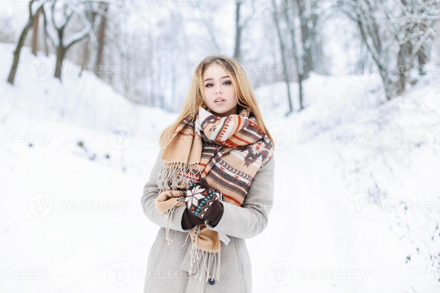 Beautiful winter portrait of a young girl with a scarf and coat on the background of snowy park photo