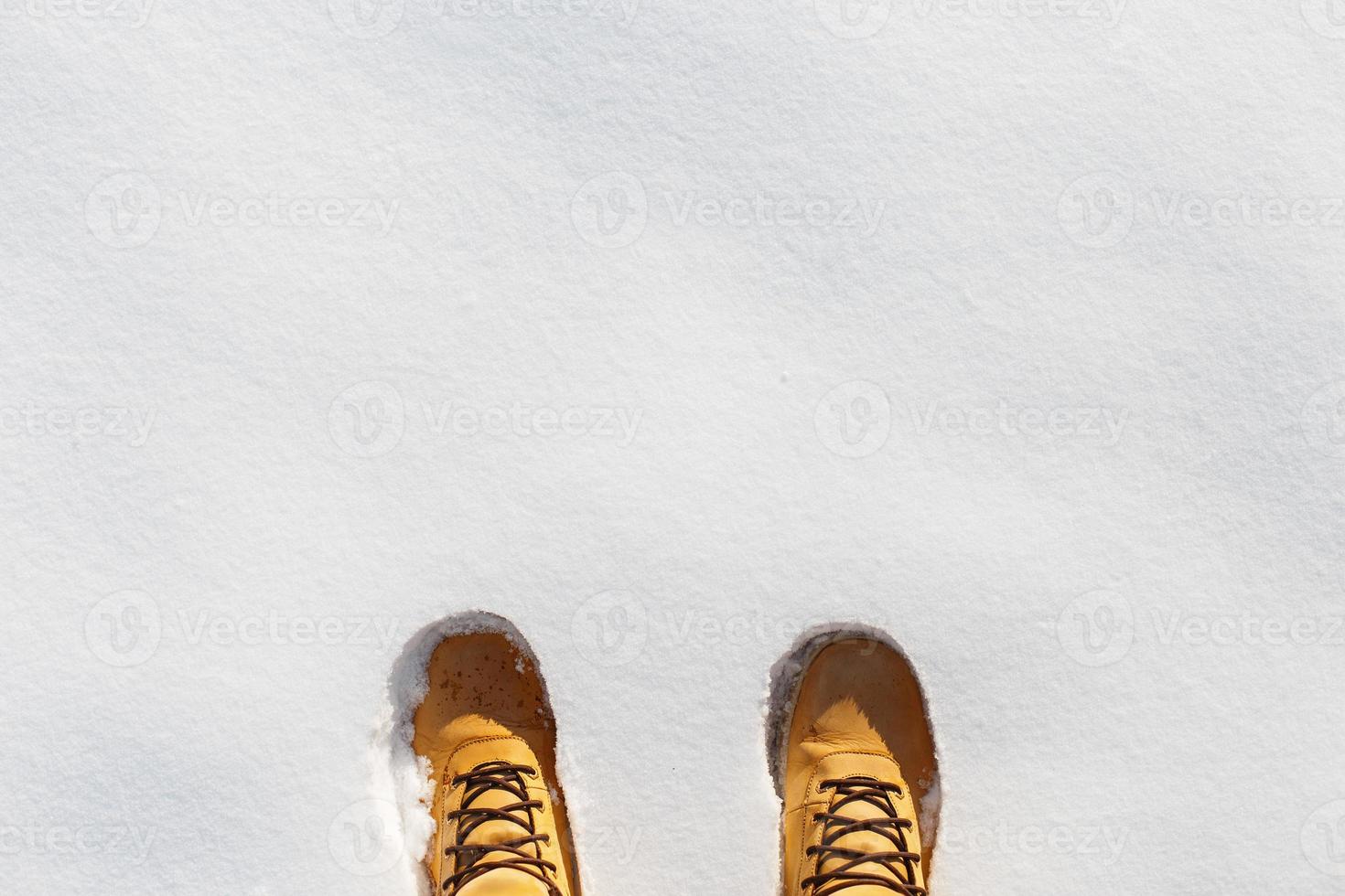 Human legs with leather yellow boots standing in the snow. Top view photo