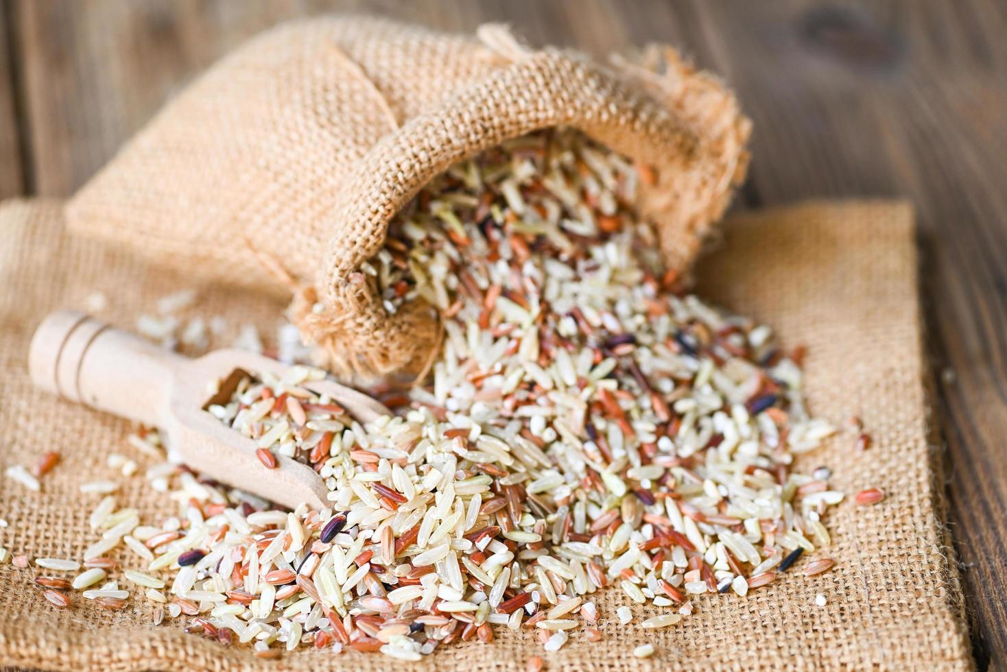 brown rice in the sack with wooden background , raw various rice color mixed thai rice for cooking food , Loonzain rice brown black red white purple health food. photo