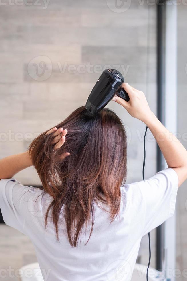 young woman using hair dryer at home or hotel. Hairstyles and lifestyle concepts photo