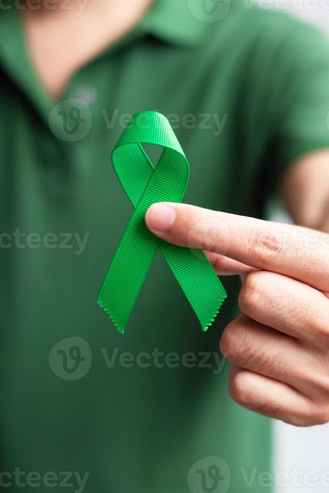 mano que sostiene la cinta verde para el hígado, las vesículas biliares, las vías biliares, el cuello uterino, el cáncer de riñón y el mes de concientización sobre el linfoma. concepto de salud y día mundial del cáncer foto