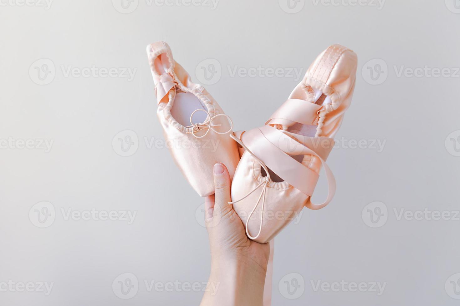 Ballerina dancer hand holding new pastel beige ballet shoes with satin ribbon isolated on white background. Ballerina classical pointe shoes for dance training. Ballet school concept. Copy space. photo