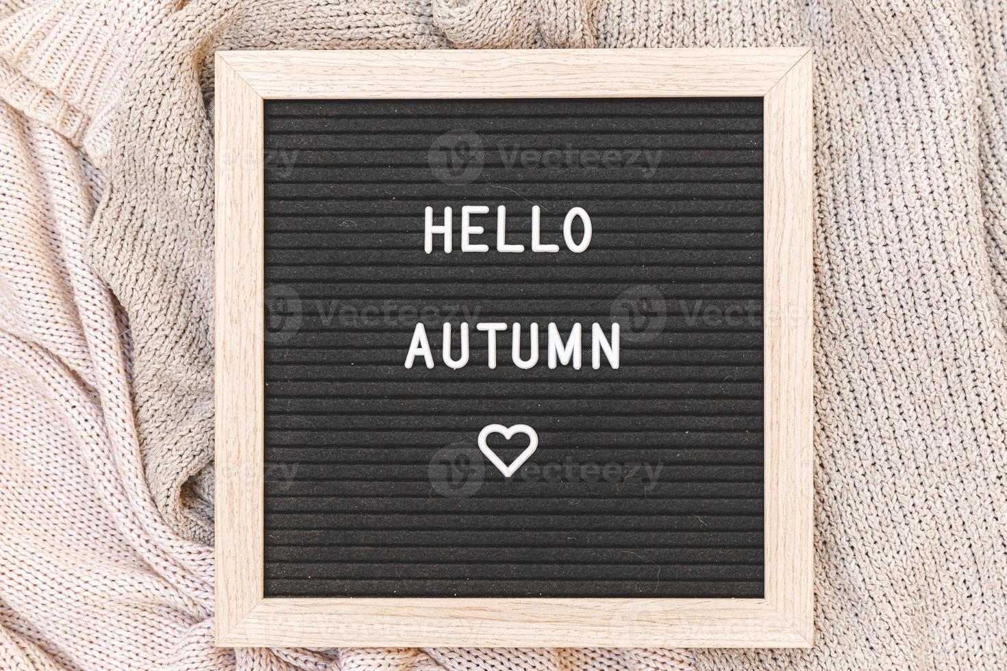 Autumnal Background. Black letter board with text phrase Hello Autumn lying on white knitted sweater. Top view, flat lay. Thanksgiving banner. Hygge mood cold weather concept photo