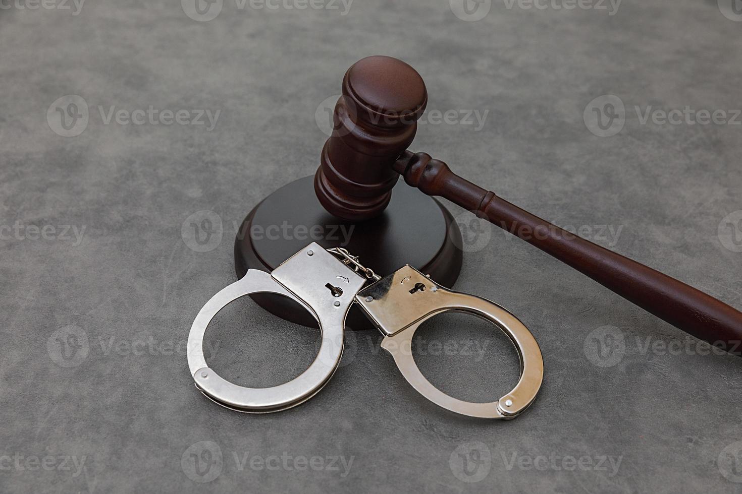 Law theme. Court of law trial in session. Judge gavel handcuffs on grey table in lawyer office or court session. Mallet of judge on concrete stone grey background. Justice human rights concept. photo