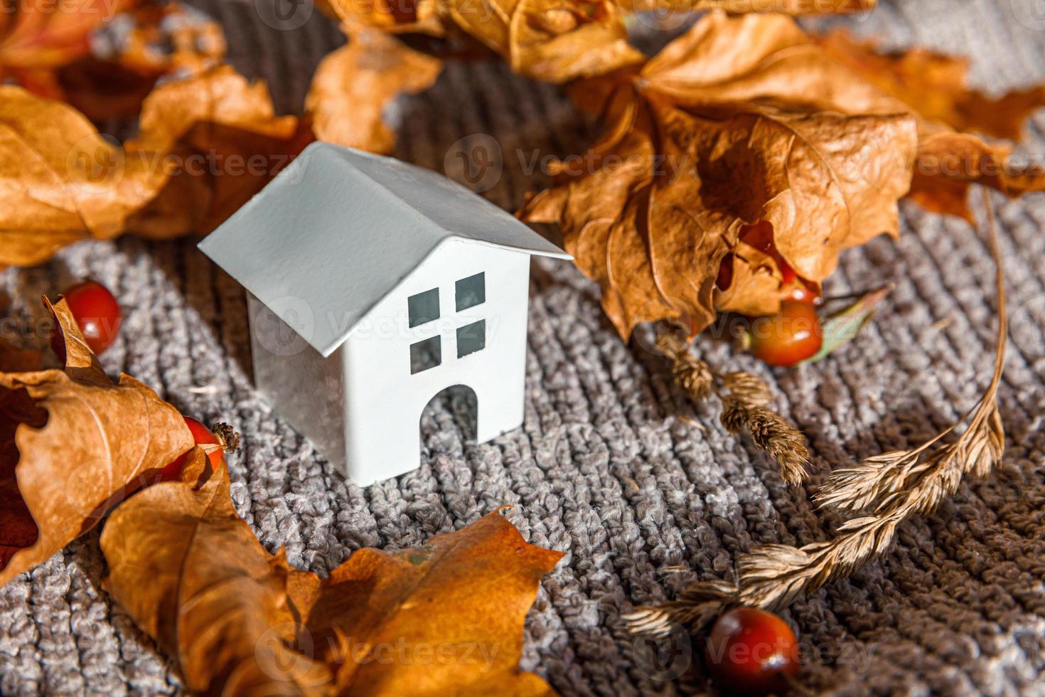 Autumnal Background. Toy house and dried orange fall maple leaves on grey knitted sweater. Thanksgiving banner copy space. Hygge mood cold weather concept. Hello Autumn with family photo