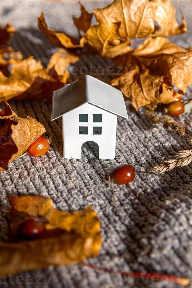 Autumnal Background. Toy house and dried orange fall maple leaves on grey knitted sweater. Thanksgiving banner copy space. Hygge mood cold weather concept. Hello Autumn with family photo