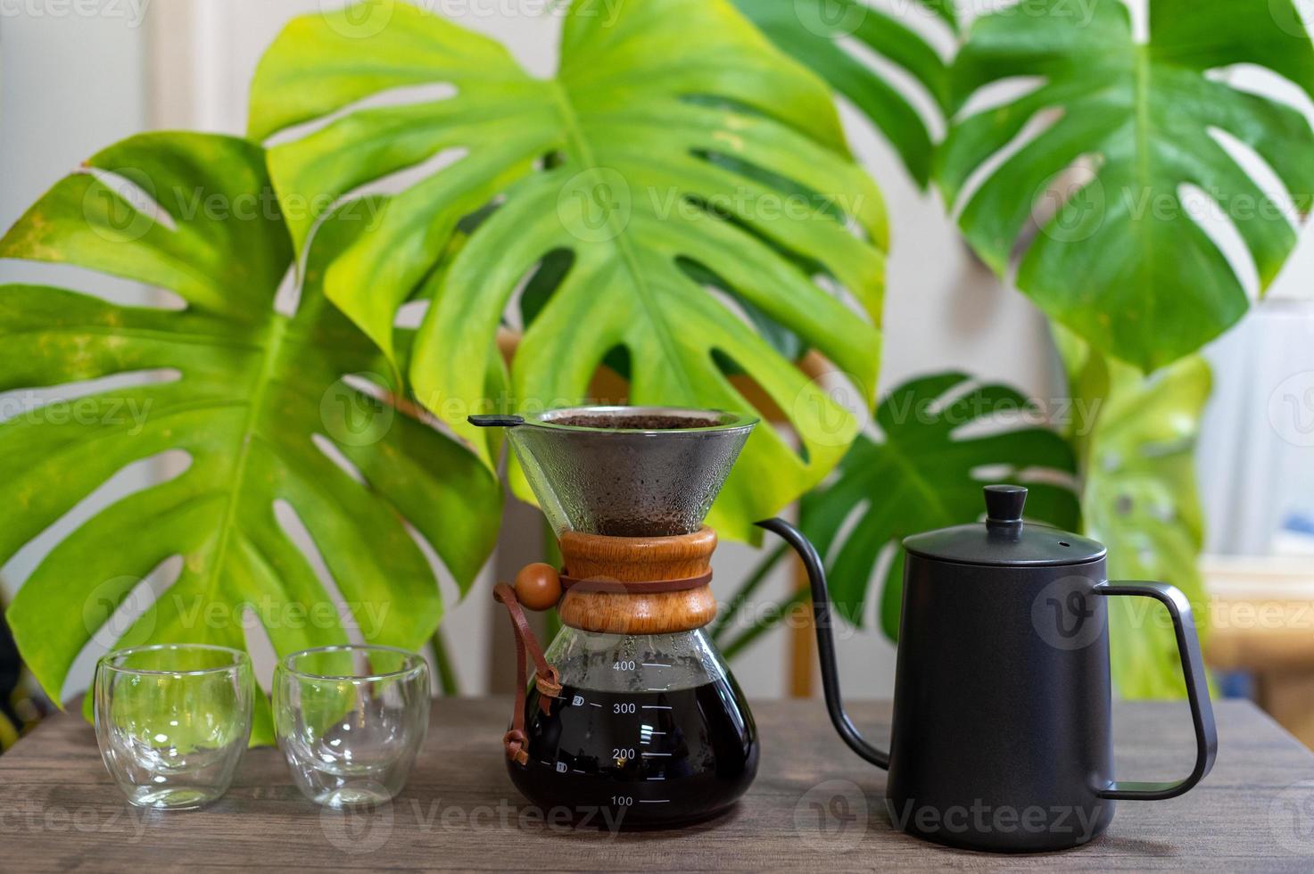 Drip coffee equipments on wooden table with monstera leaves photo