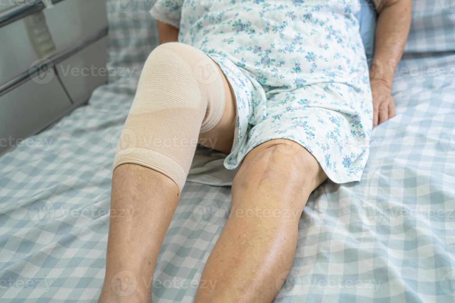 Asian senior or elderly old lady woman patient with knee support pain joint on bed in nursing hospital ward, healthy strong medical concept. photo