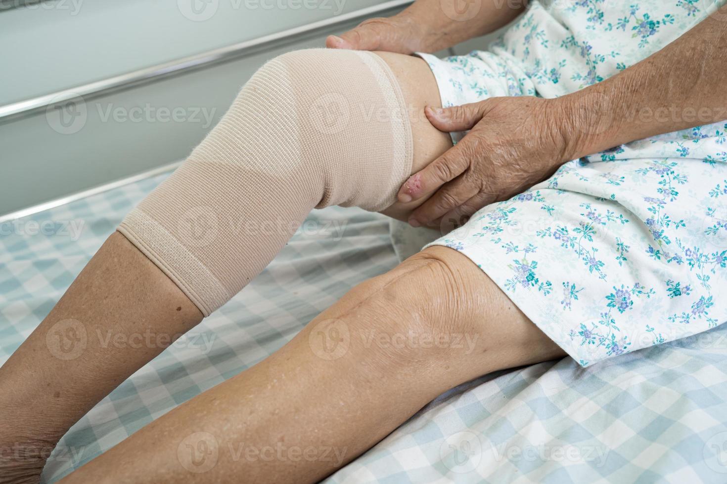 Asian senior or elderly old lady woman patient with knee support pain joint on bed in nursing hospital ward, healthy strong medical concept. photo