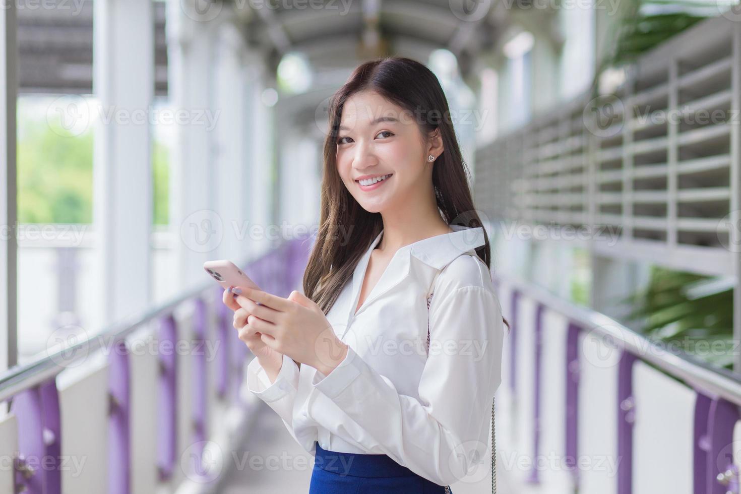 Asian beautiful business female stands on flyover of skytrain in town while uses her smartphone to send messages to customers. photo