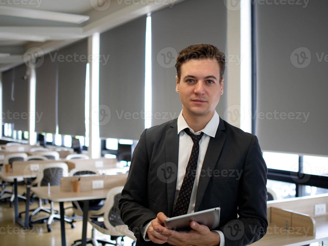 Businessman manager executive indoor company office looking at camera hold tablet technology electronic work job career wirelesss network online digital.Male smart handsome person stand happy smile photo