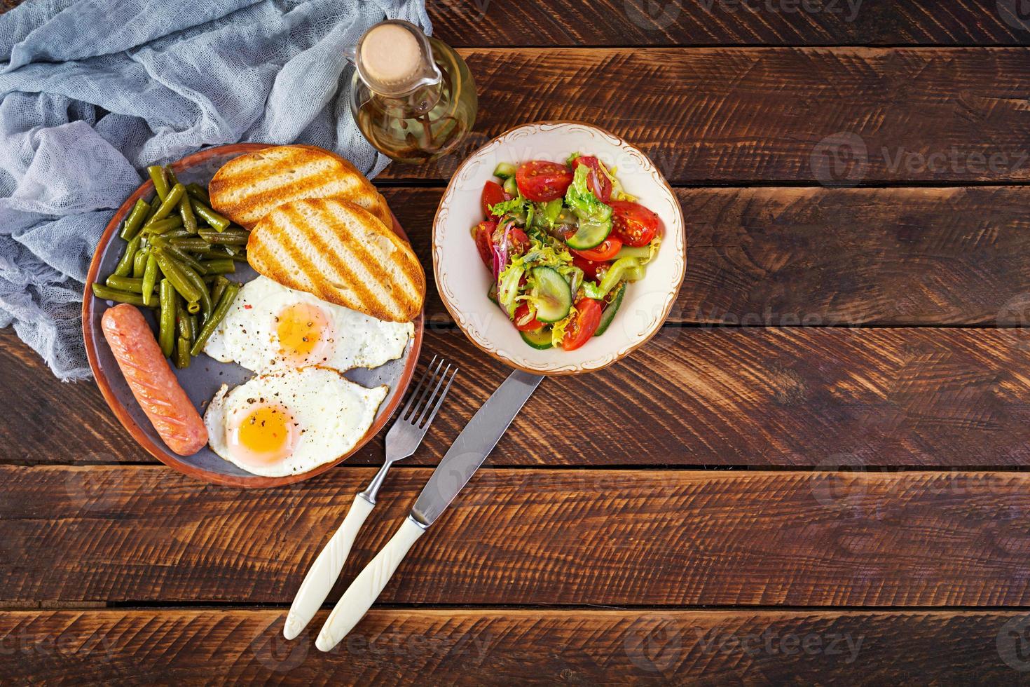 Breakfast with eggs, grilled sausage, green beans and toast on wooden background photo