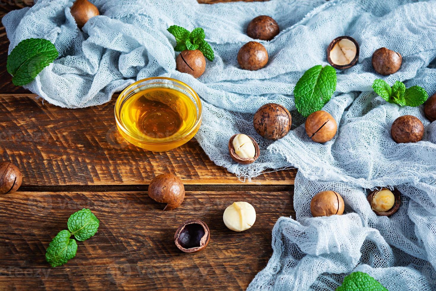 nueces de macadamia con cáscara con hojas de menta y miel sobre fondo de madera foto