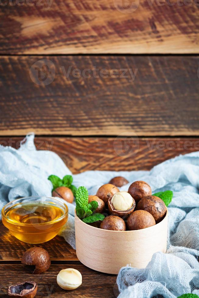 Macadamia nuts in shell with mint leaves and honey on wooden background photo