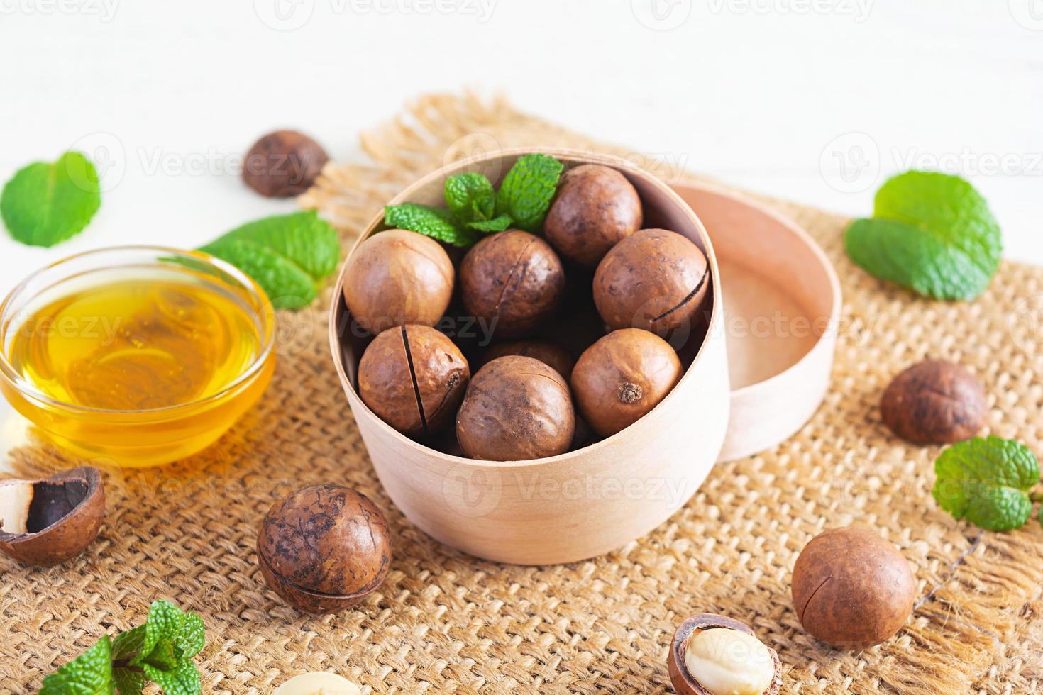 Macadamia nuts in shell with mint leaves and honey on wooden background photo