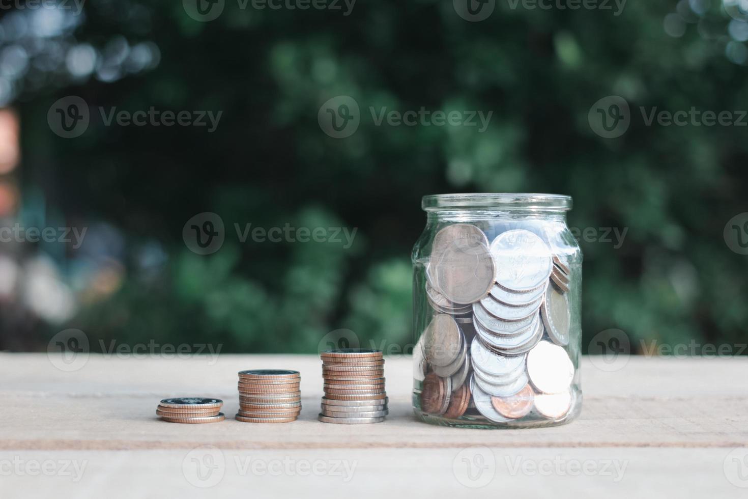 Coins in clear jar placed on wooden planks outdoors in the garden, investment saving concept.copy space. photo