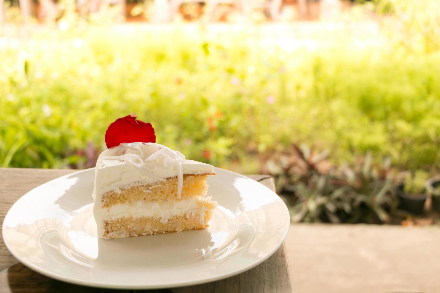 A piece of coconut cake on white plate with green garden background. photo