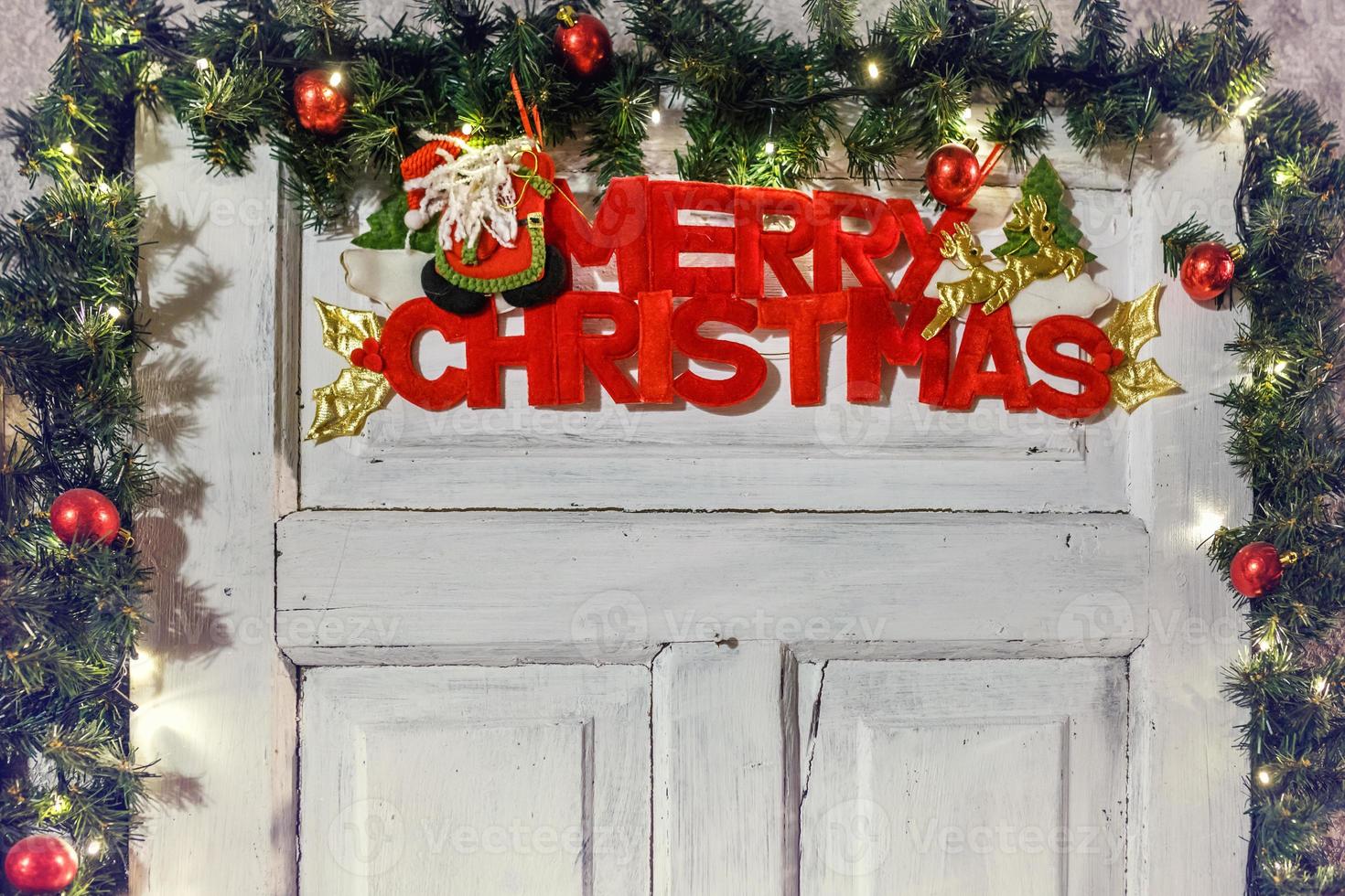 the inscription of a merry christmas on a white wooden door, surrounded by fir branches and toys photo