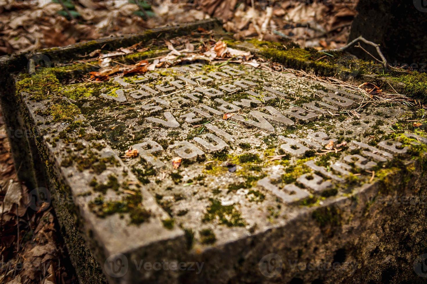 antigua lápida de la primera guerra mundial cubierta de musgo y hojas viejas en el bosque de otoño foto