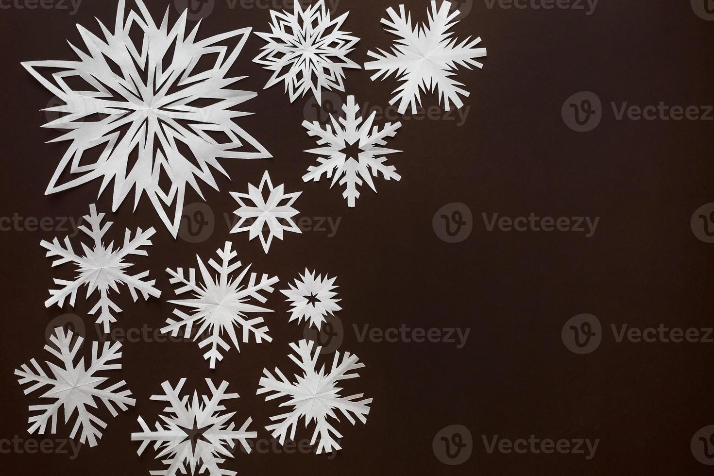 White paper snowflakes different shapes and sizes on brown cardboard background. Top view. photo