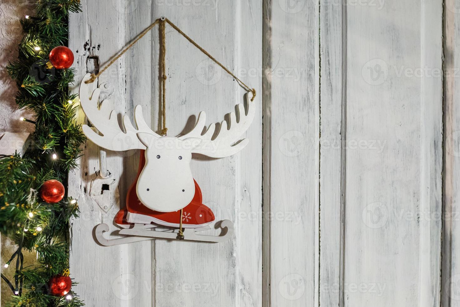 wooden toy moose elk skates in a Santa Claus costume hanging on a wall surrounded by fir and rowan tree branches photo