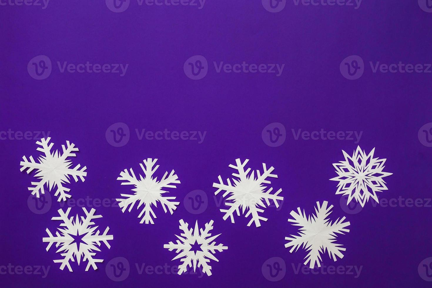 White paper snowflakes different shapes and sizes on violet background. Top view. photo