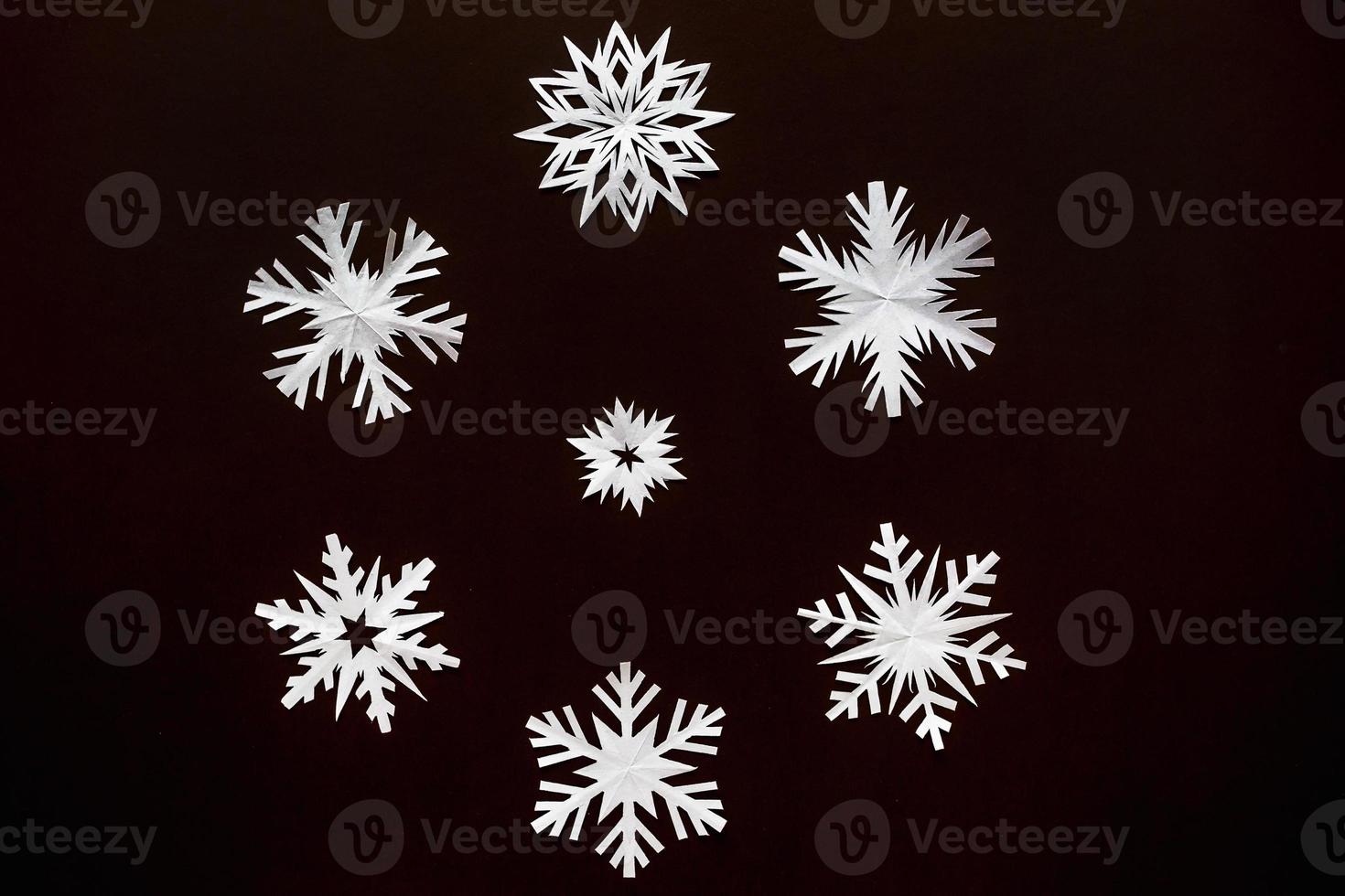 White paper snowflakes different shapes and sizes on brown cardboard background. Top view. photo