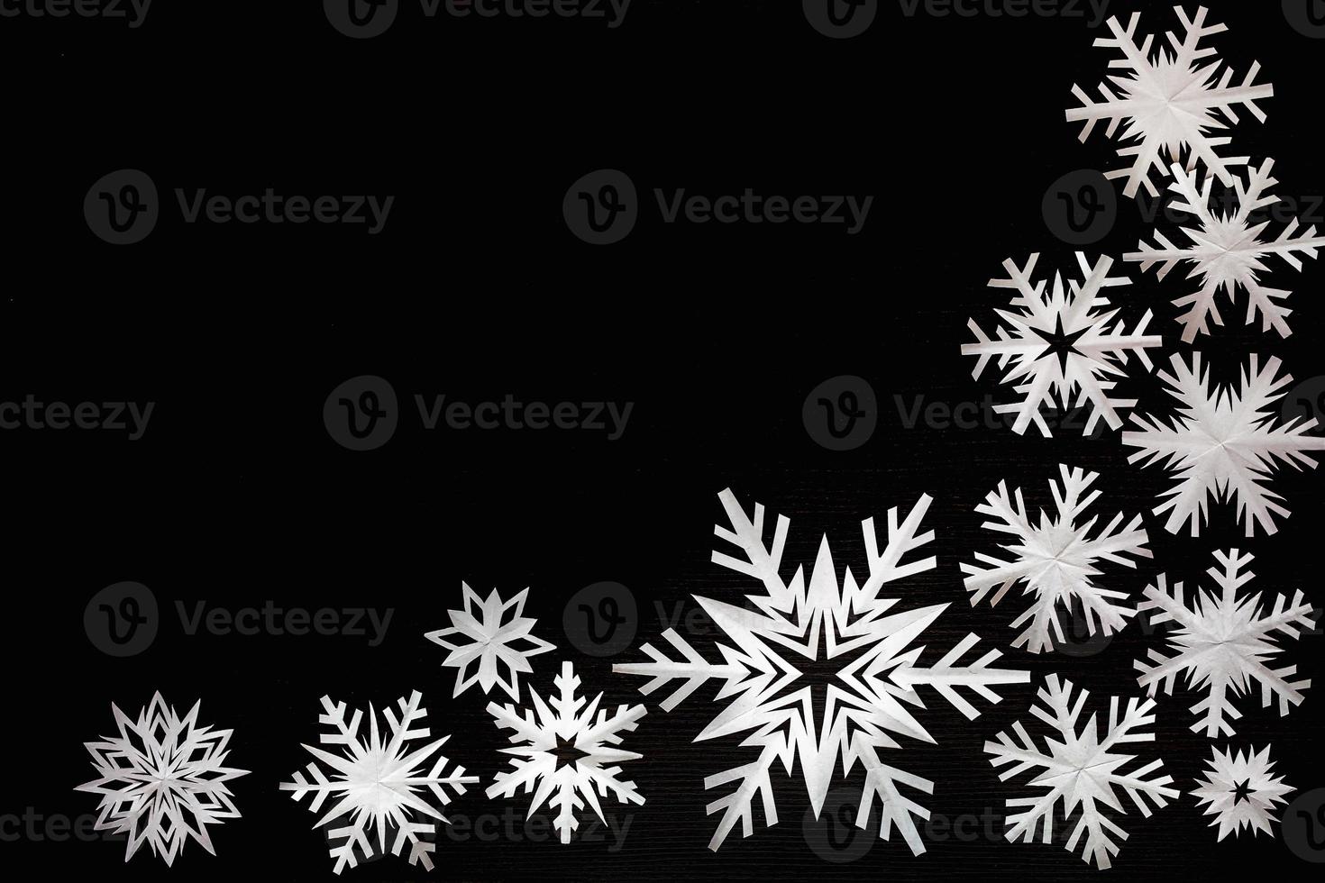 White paper snowflakes different shapes and sizes on black cardboard background. Top view. photo