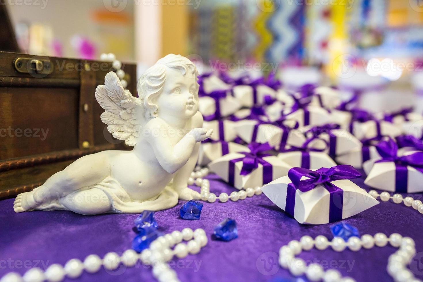 ceramic angel on the table with a violet tablecloth and small gifts for guests from the newlyweds photo