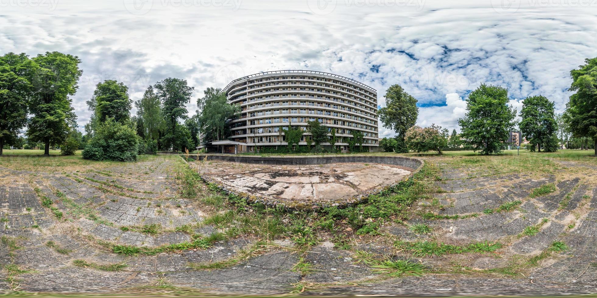 full seamless panorama 360 by 180 degrees angle view facade of  abandoned multi-storey, collapsing hotel near dry empty fountain in equirectangular spherical equidistant projection. VR AR content photo