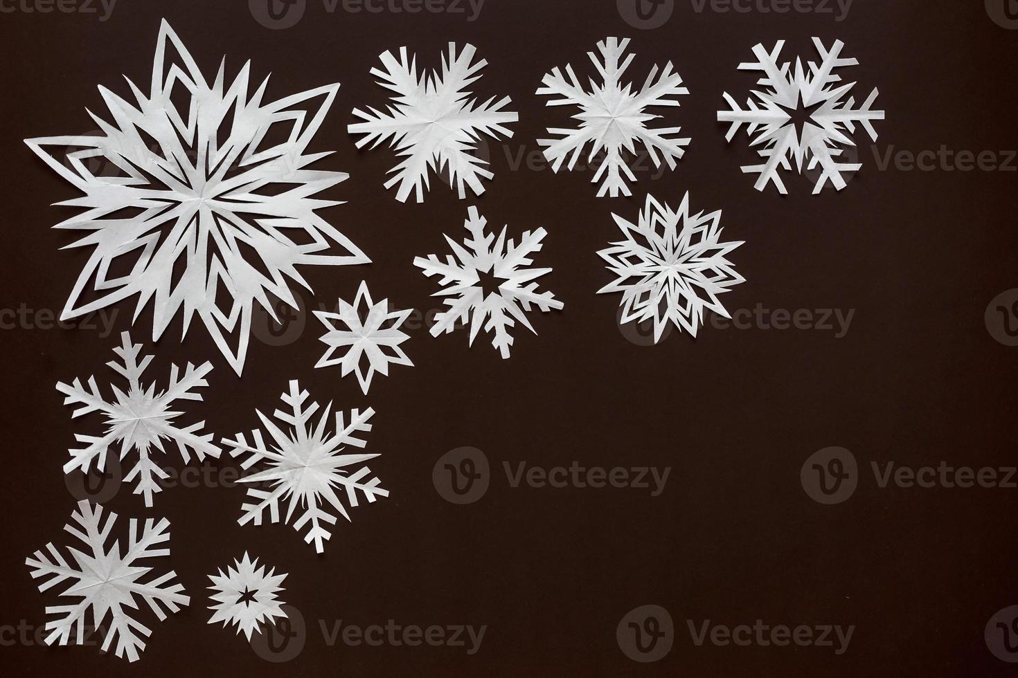 White paper snowflakes different shapes and sizes on brown cardboard background. Top view. photo