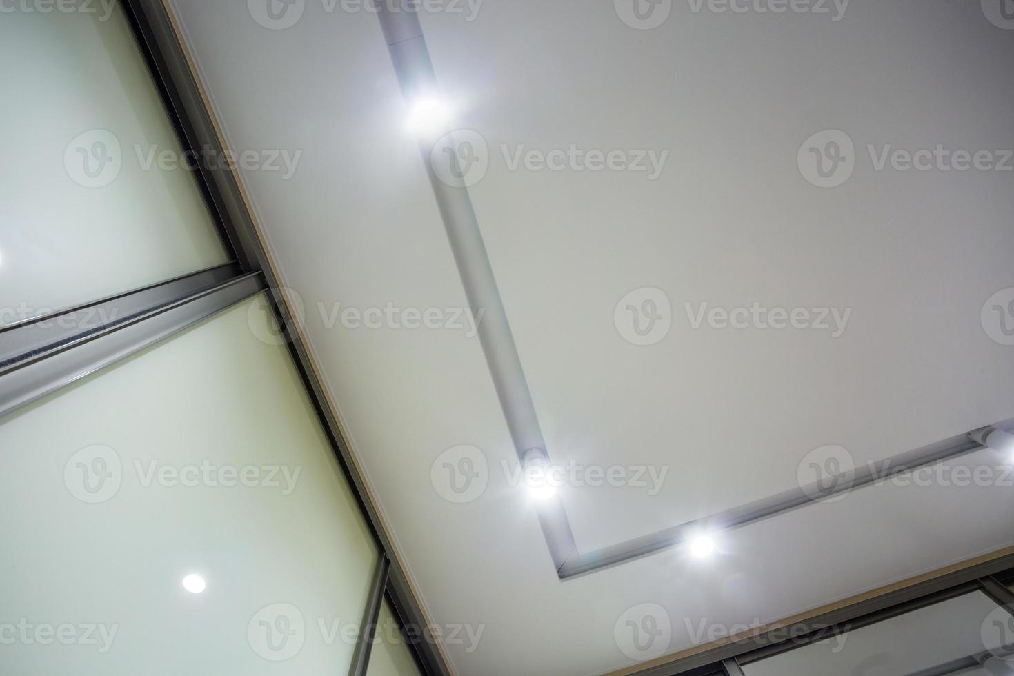 halogen spots lamps on suspended ceiling and drywall construction in in empty room in apartment or house. Stretch ceiling white and complex shape. photo