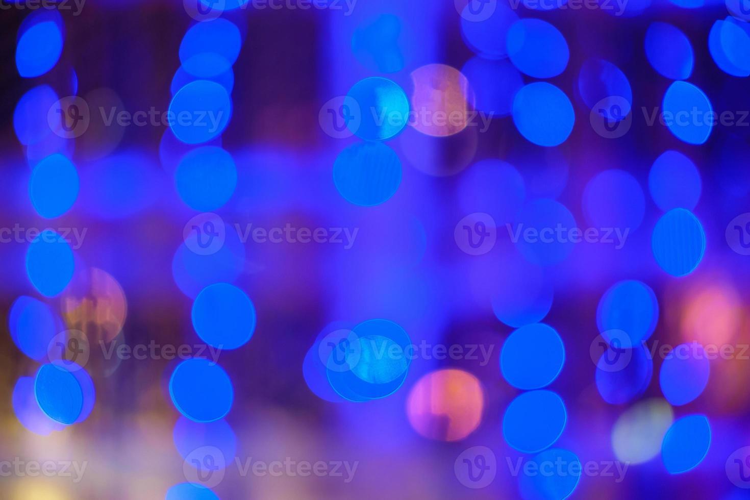 Blurred bokeh colorful lights lanterns, holiday new year lighting on black background Christmas winter glitter shiny light bokeh in rainbow colors. Holiday purple blue pink violet natural texture. photo