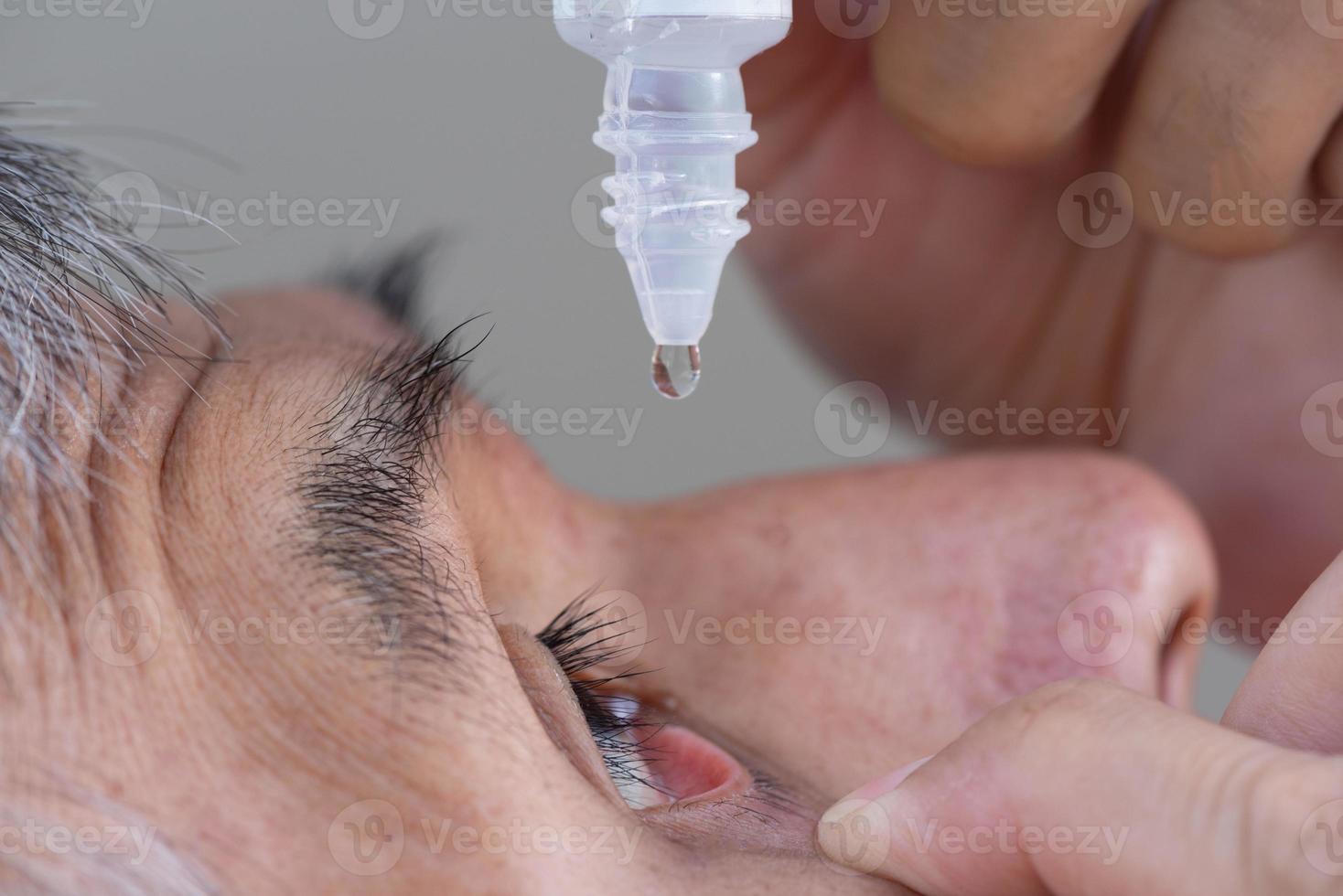 A senior Asian man using eye drop in right eye photo