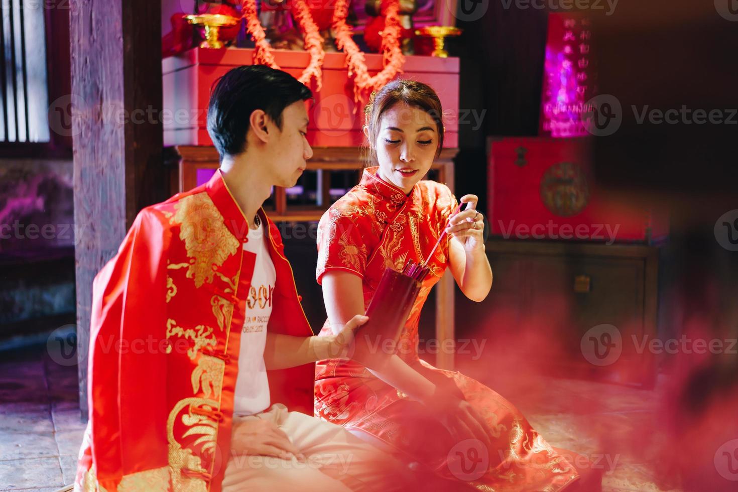 feliz joven pareja asiática con vestidos tradicionales chinos rezando en el templo foto