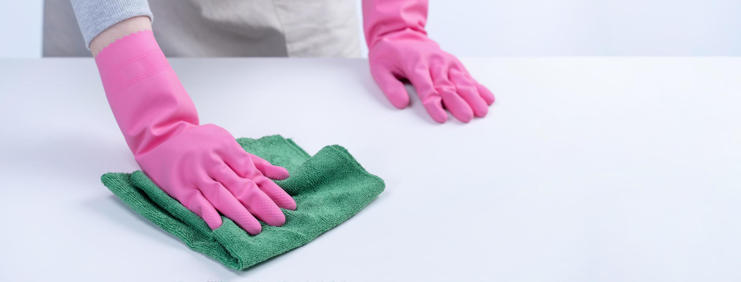 mujer ama de llaves con guantes protectores y trapo para limpiar la superficie de la mesa. foto