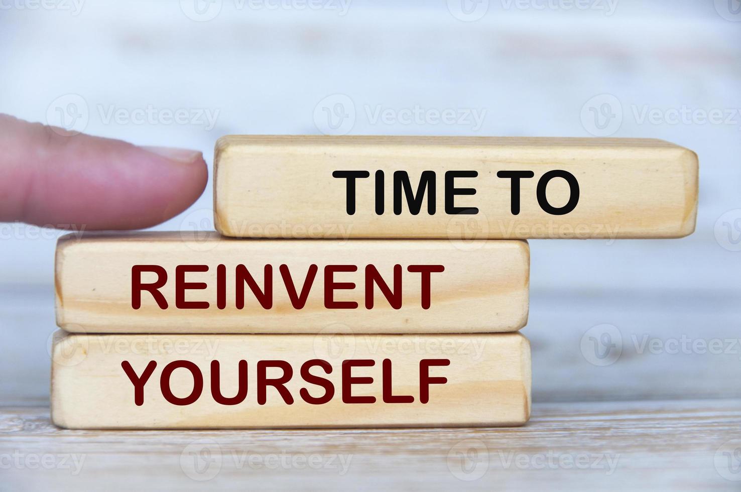 Finger pushing wooden blocks with text - Time to reinvent yourself. photo