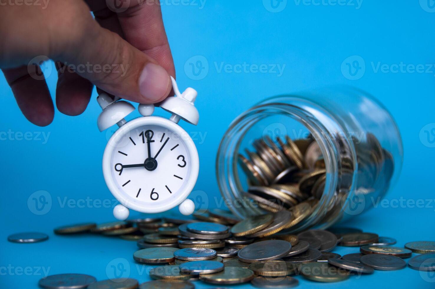 Scattered gold coins with hand holding alarm clock. Business concept photo