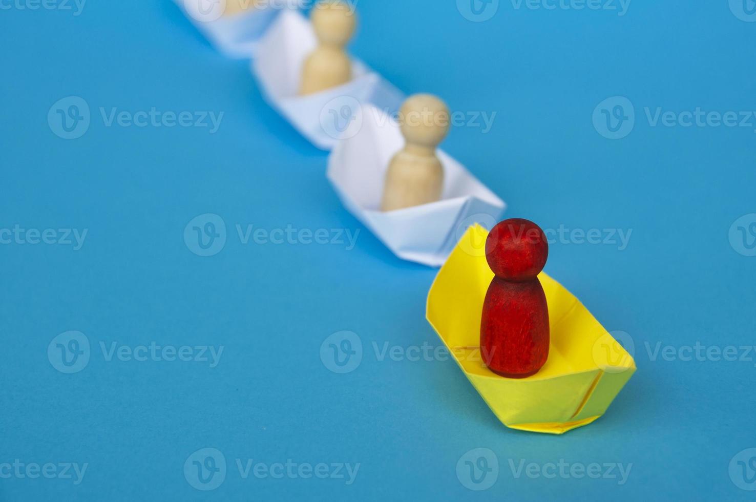 Leadership Concept - Red wooden figure on yellow paper ship origami leading the rest of the figure on white paper ship. photo