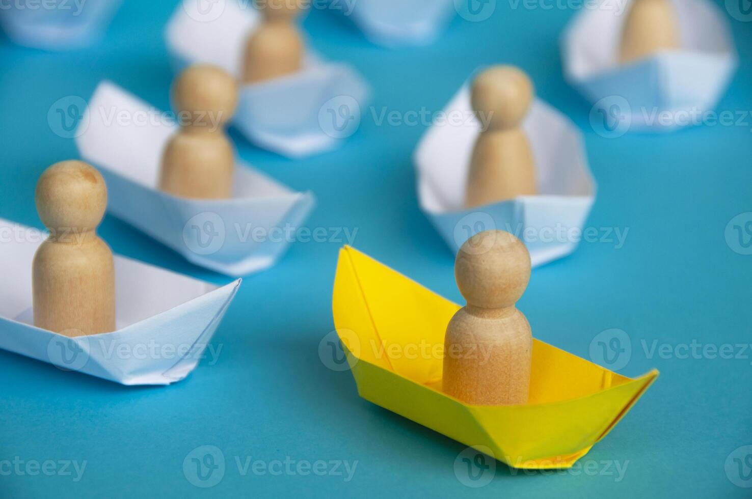 Leadership Concept - Wooden figure on yellow paper ship origami leading the rest of the figure on white paper ship. photo