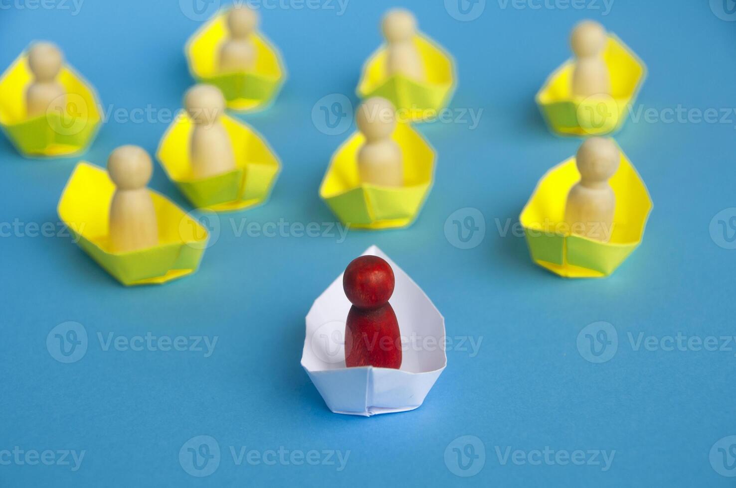 Leadership Concept - Wooden figure on white paper ship origami leading the rest of the figure on yellow paper ship. photo