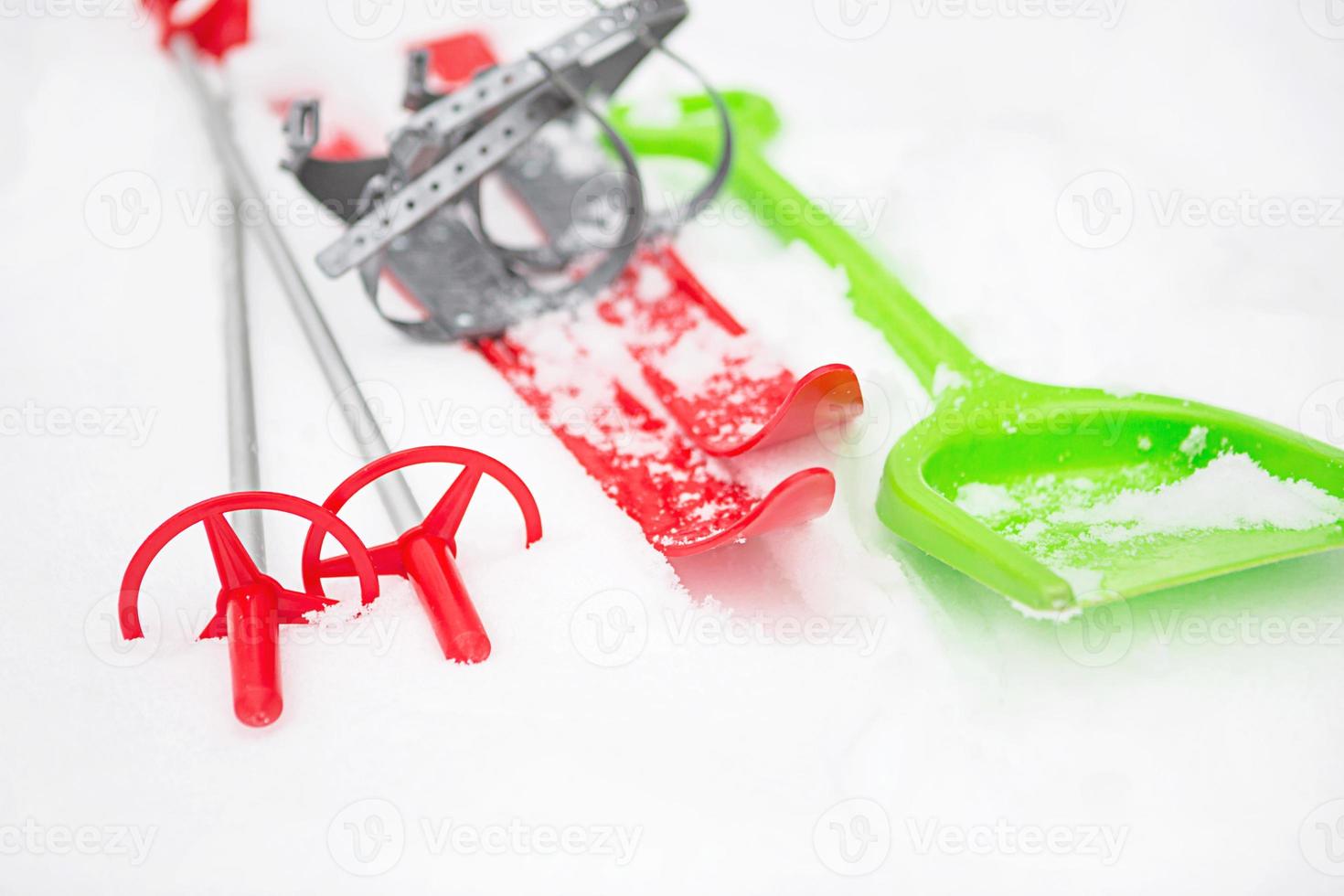 Children's red skis with sticks and a green snow shovel-layout in the snow. Winter outdoor activities, family fun. White natural frosty background. Copy space photo